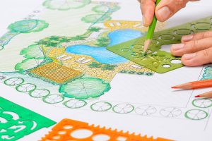 Landscape designer creating a backyard pond layout with colored pencils and templates on a detailed site plan.
