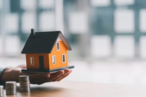 Model house with stacked coins symbolizing how backyard water features increase property value.