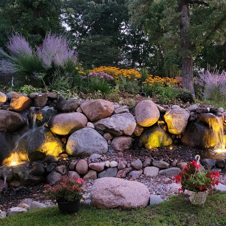 Natural stone waterfall illuminated with warm lighting at dusk